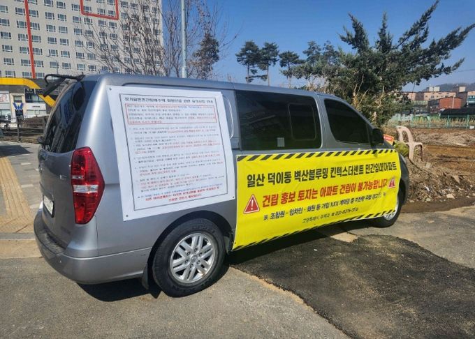 승합차에 게시된 덕이동 민간임대 주택 건립 불법 모집 경고 현수막