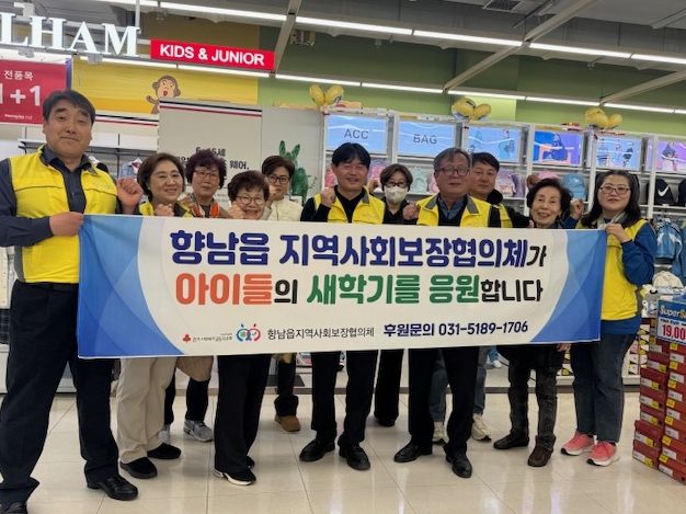 향남읍지역사회보장협의체 위원들이 ‘새 학기 봄맞이 바우처’ 지원사업 현수막을 들고 기념촬영을 하고 있다